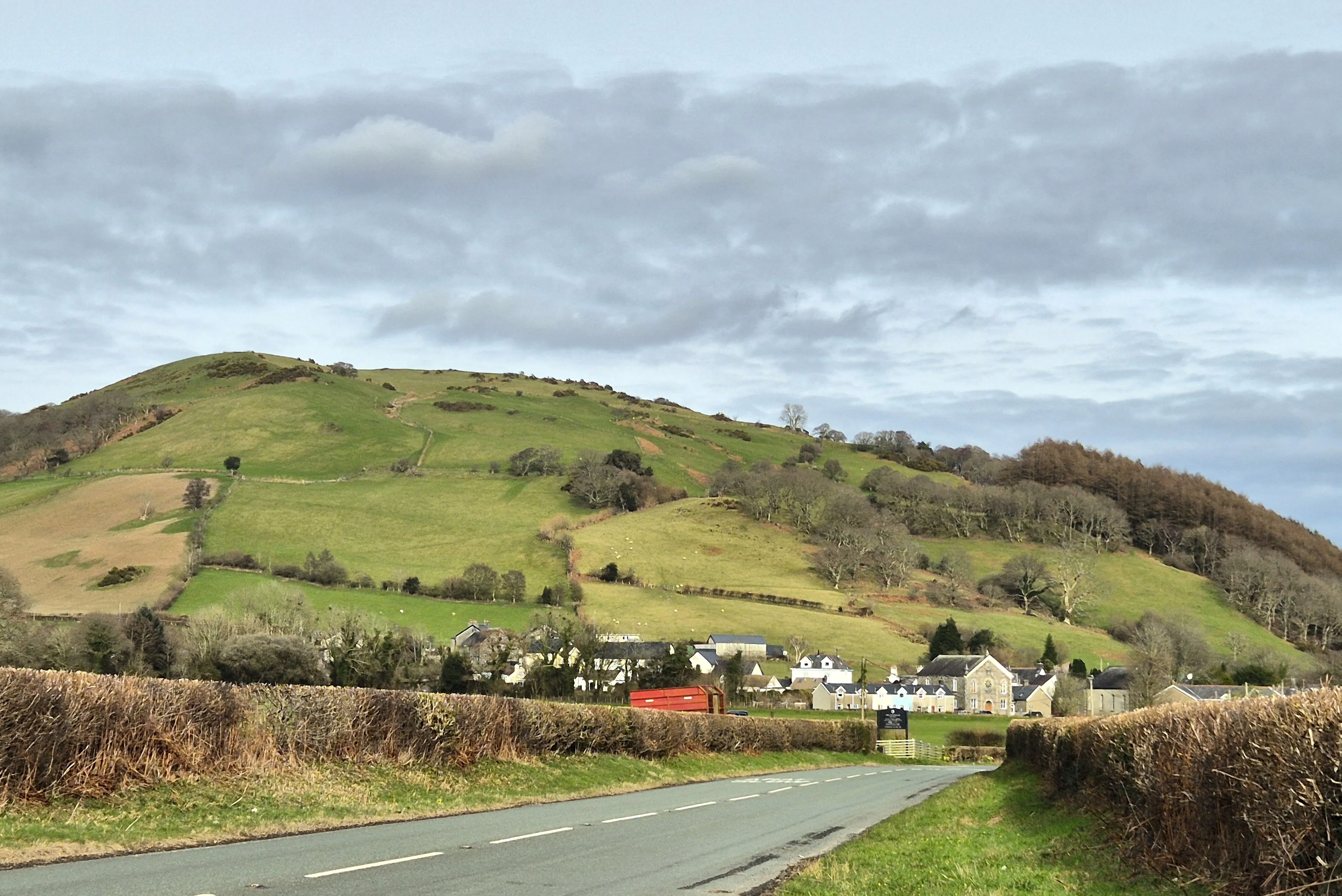 Rural Mid-Wales road leading toward a village at the foot of a green hill