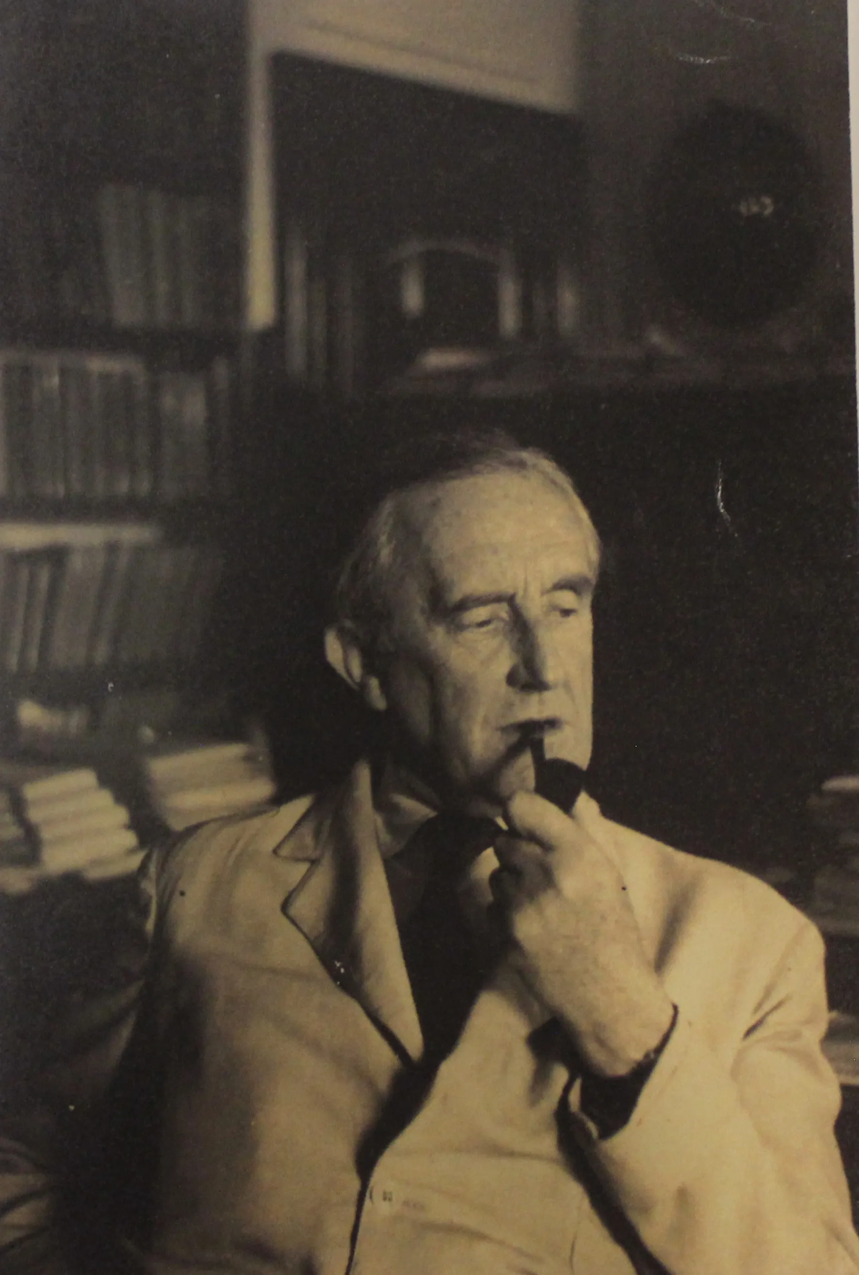Sepia portrait of J.R.R. Tolkien smoking a pipe in his study, bookshelves behind